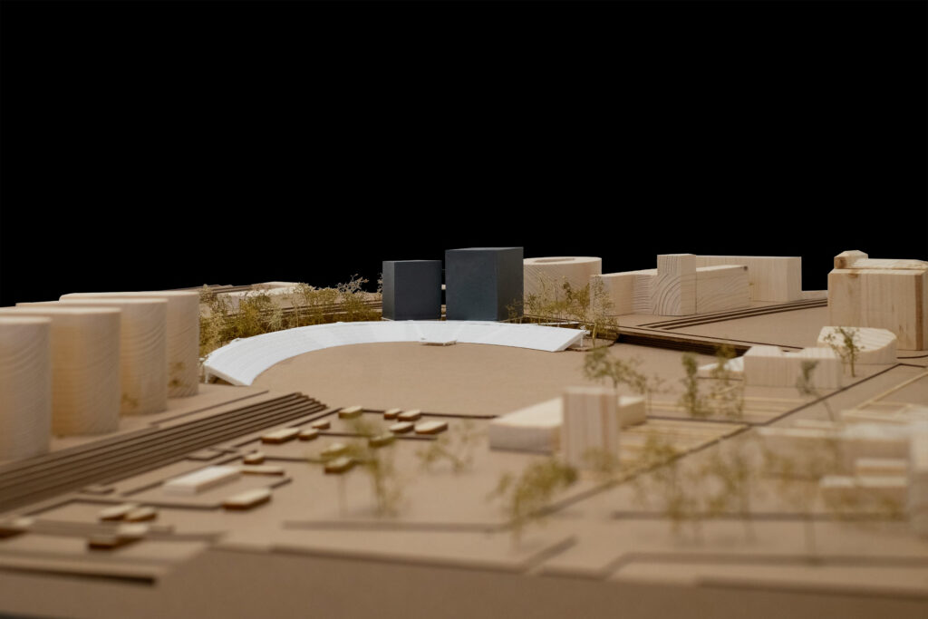 Architekturmodell von Sebastian Bendszus mit einer kreisförmigen Struktur mit zwei dunklen rechteckigen Blöcken, die an Archicad-Designs erinnern, umgeben von geometrischen Formen und Miniaturbäumen auf dunklem Hintergrund.