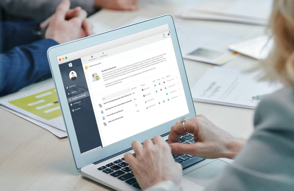 Eine Person verwendet einen Laptop, auf dem die Team-Kollaborationssoftware von Nova angezeigt wird, während andere, darunter Ava, an einem Tisch mit Dokumenten diskutieren.